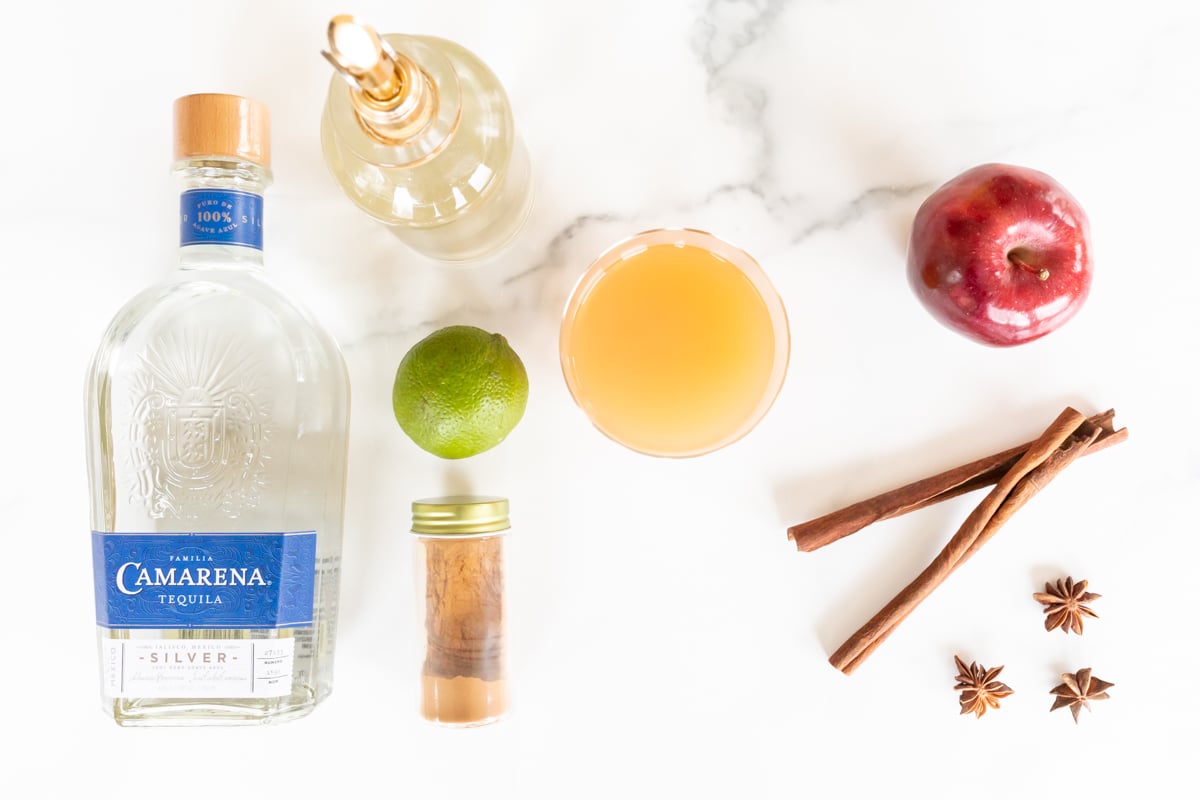 Ingredients for an apple cider margarita recipe laid out on a marble countertop.