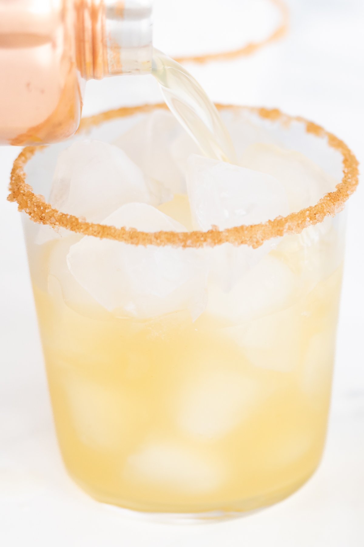 A shaker pouring an apple cider margarita into a cocktail glass.