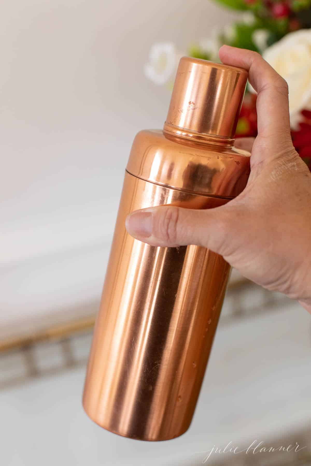 A hand holding a copper cocktail shaker.