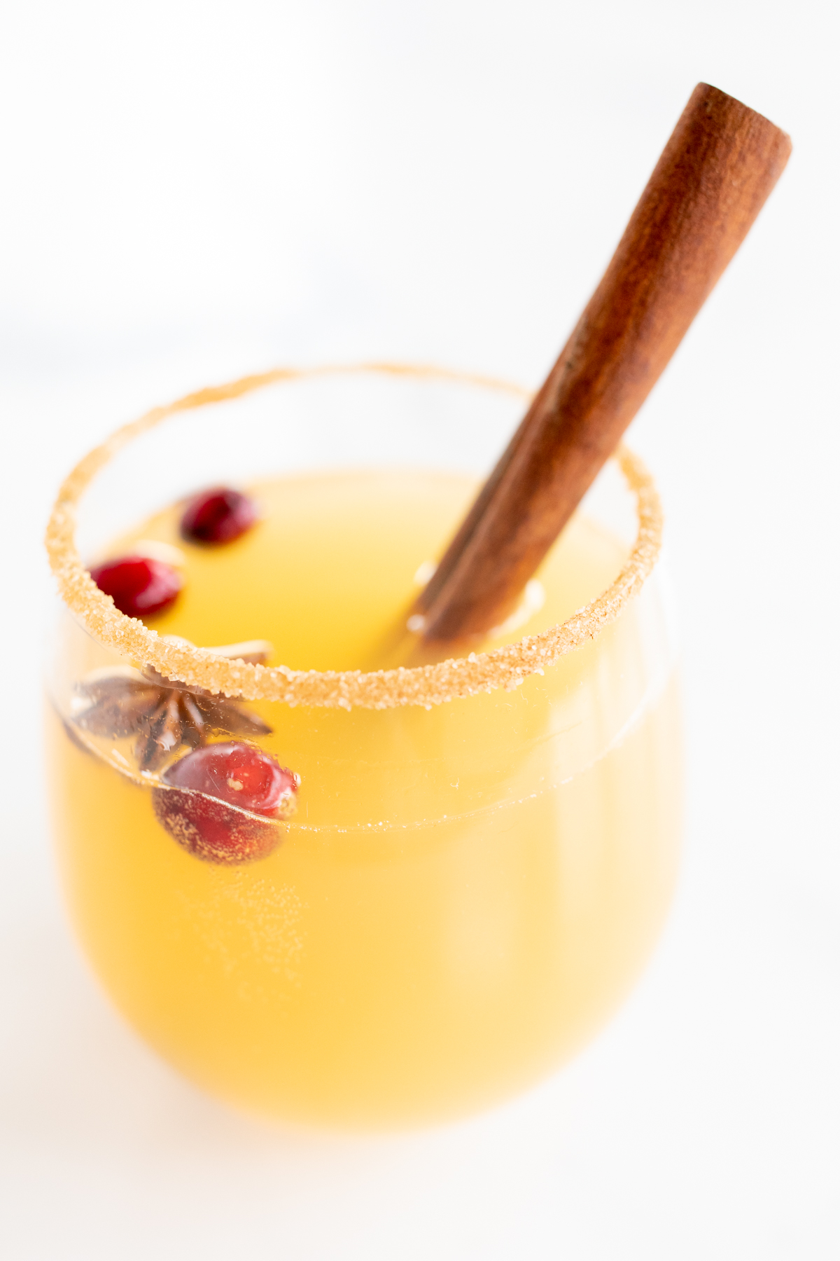 A clear glass of apple cider sangria, garnished with a cinnamon stick.