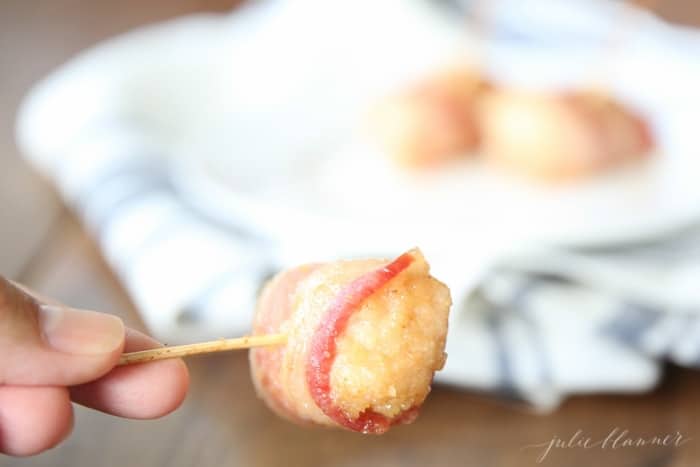 A hand with a bacon chicken hors doeuvre on a toothpick.