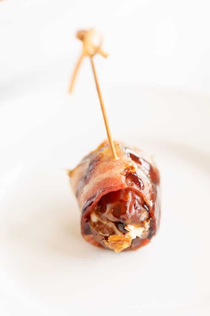 A single stuffed date on a white plate with a toothpick.
