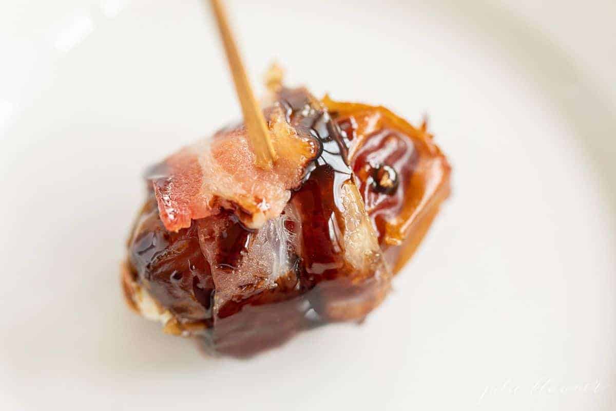 A date wrapped in bacon with a toothpick on a white surface.
