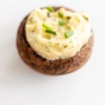 A single boursin stuffed mushroom on a white surface, topped with diced chives.