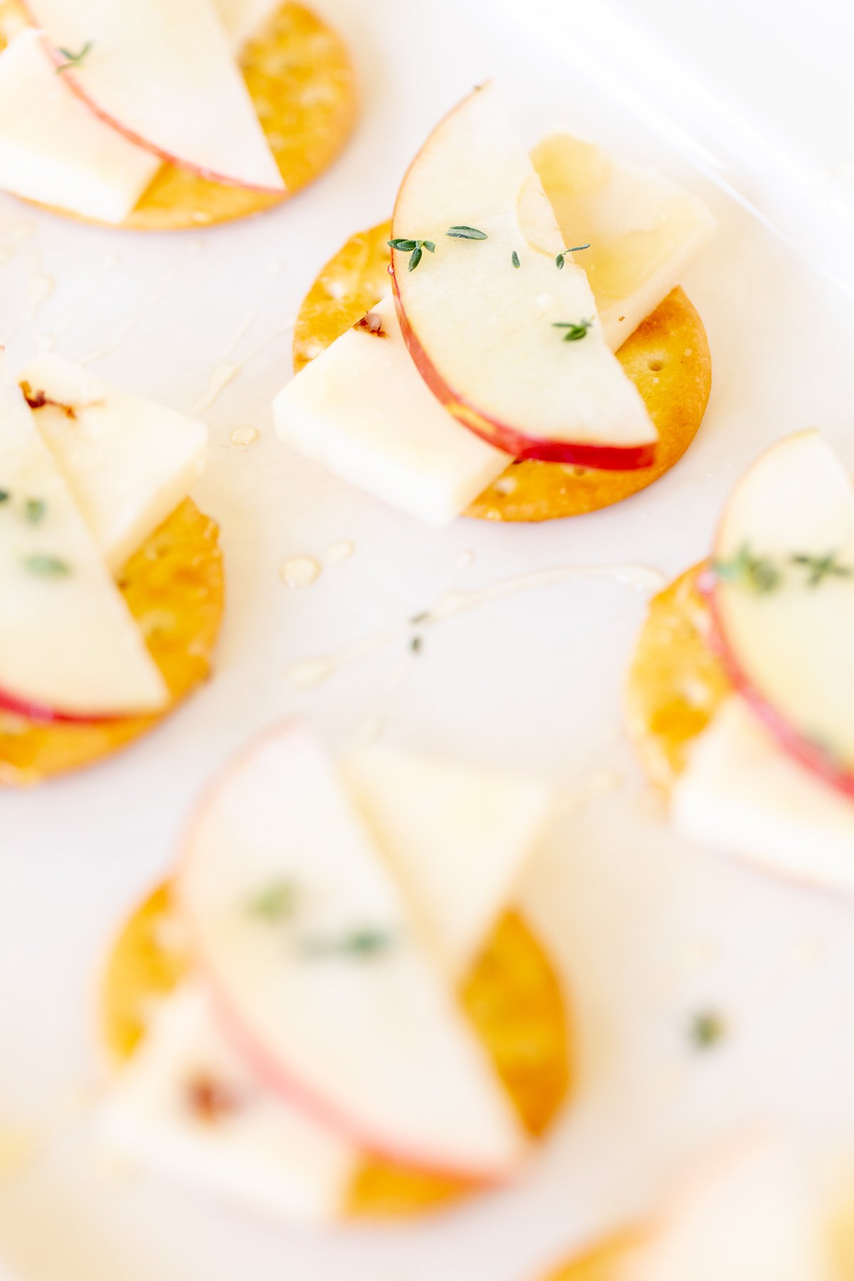 Cheese and crackers on a white platter, with an apple slice and fresh herbs.