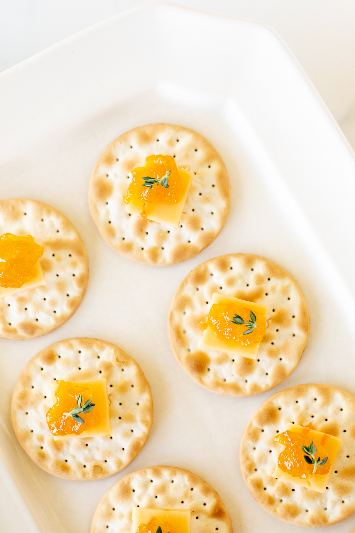 cheese and crackers topped with jelly on a white plate.