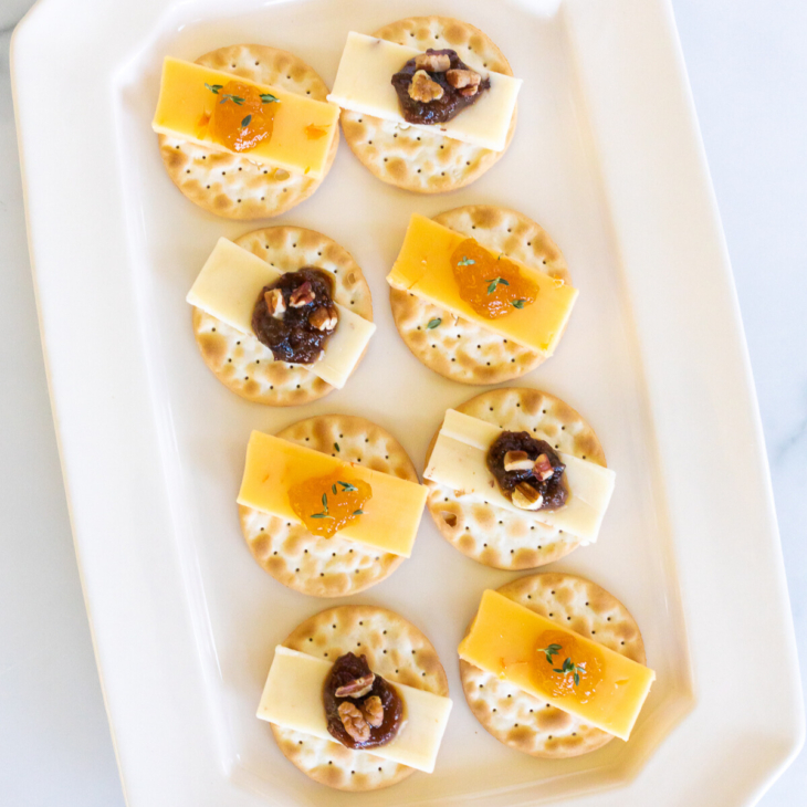 cheese and crackers topped with jelly on a white plate.