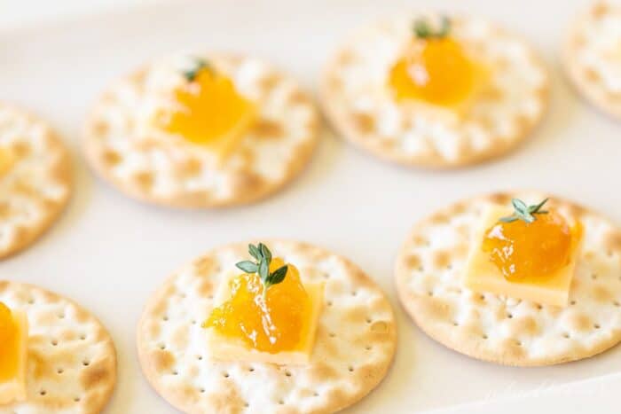 A display of individual cheese and crackers topped with jam on a white platter.
