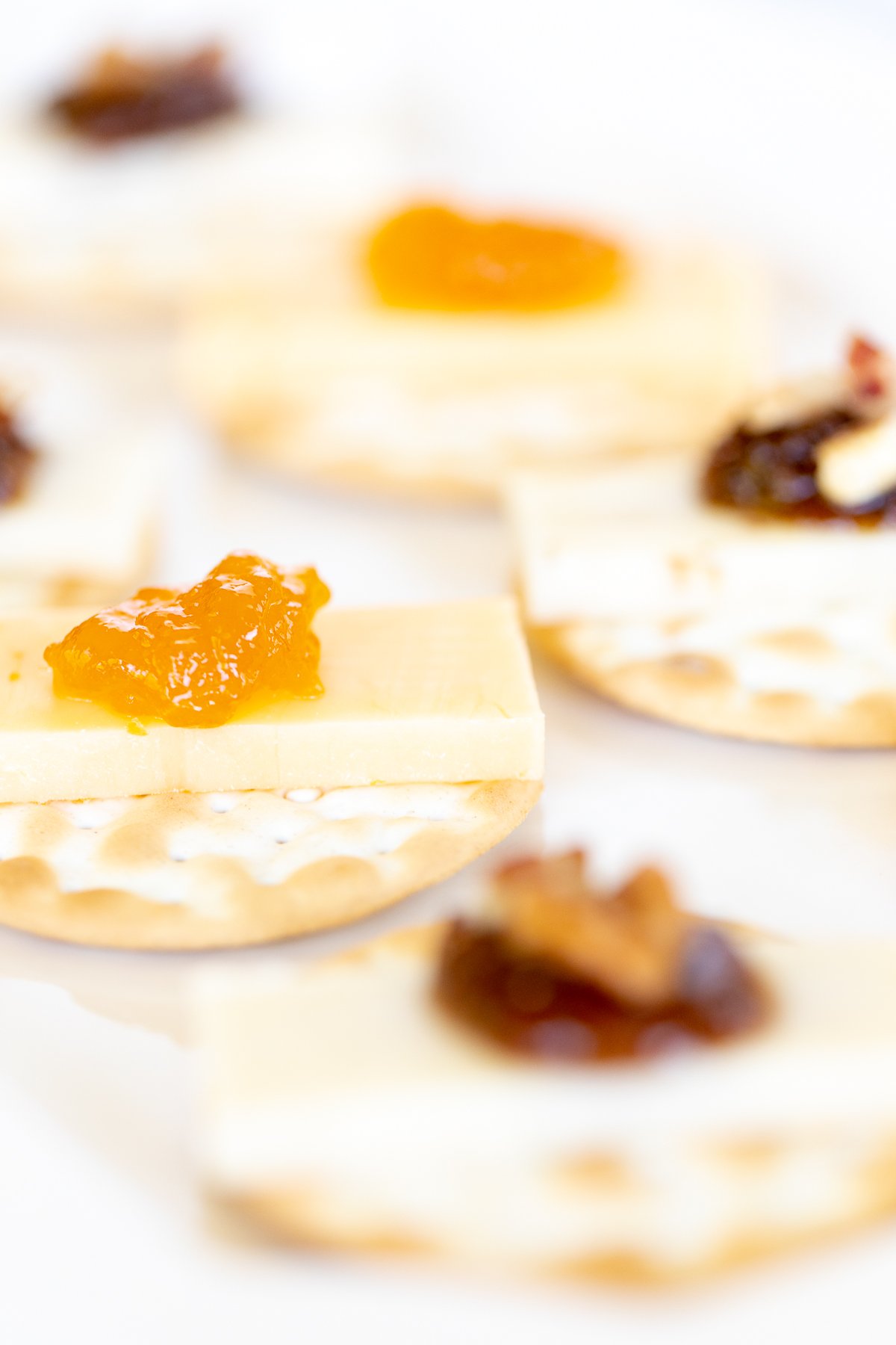 cheese and crackers topped with jelly on a white plate.