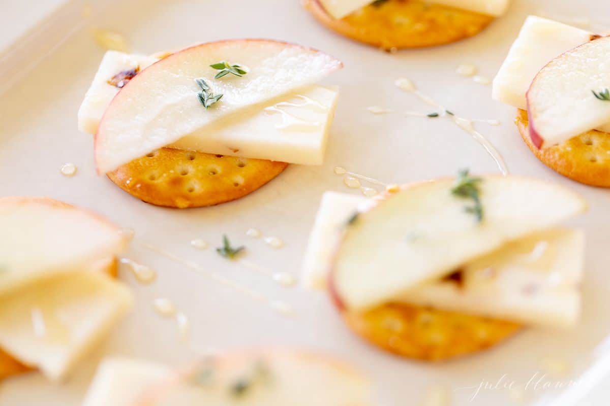 Cheese and crackers displayed on a white platter with slices of apples on top.