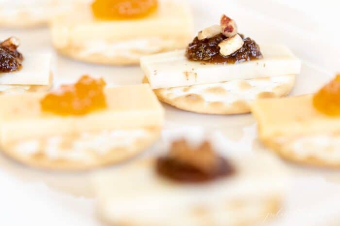 A display of individual cheese and crackers topped with jam on a white platter.
