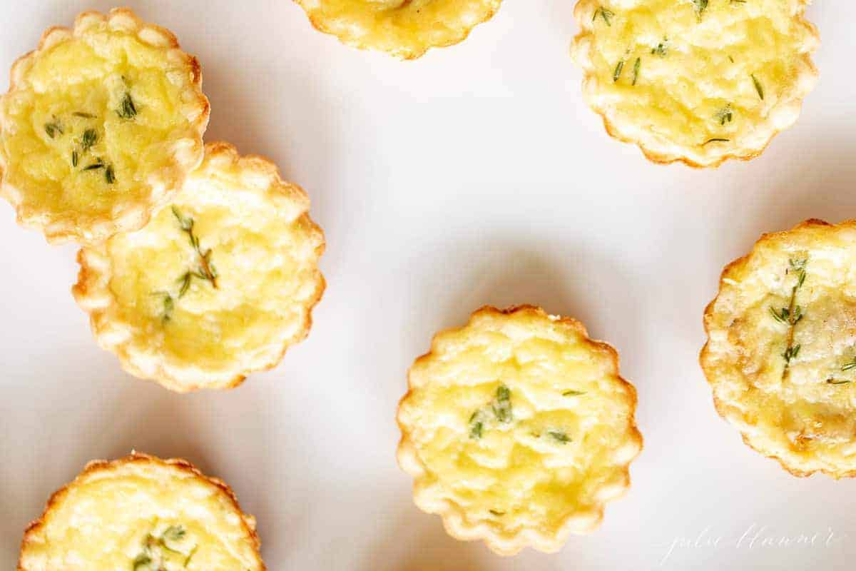 Mini cheese tart hors d'oeuvres on a white surface.
