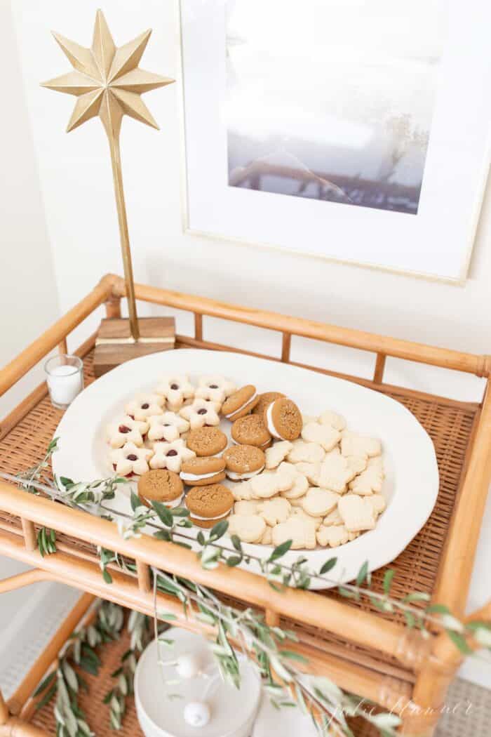 A bamboo bar cart with a white oval platter filled with Scandinavian Christmas cookies, fresh greenery accents.