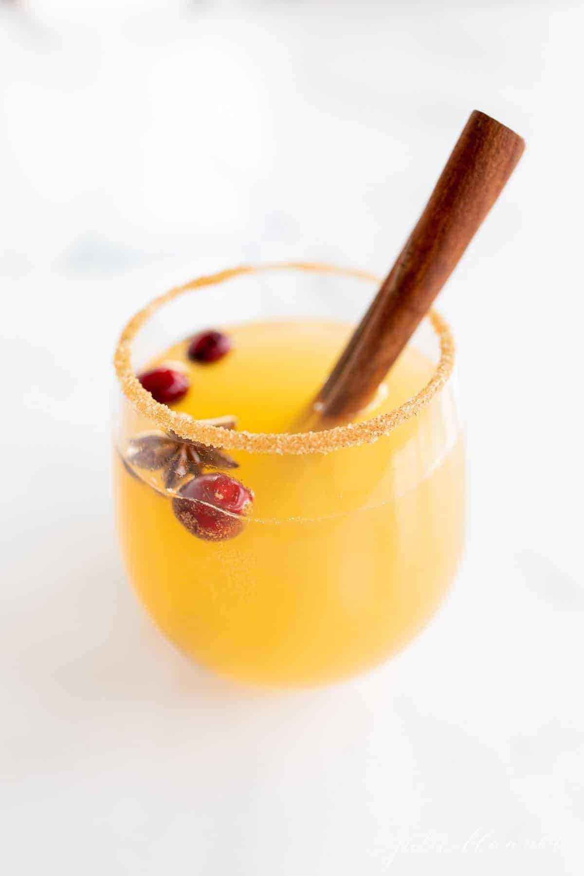 A clear glass full of Christmas sangria with cranberries and a cinnamon stick.