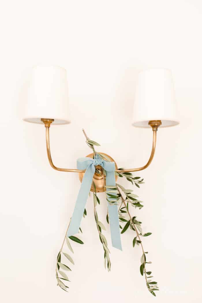 A brass two branch wall sconce with a touch of olive branch tied on with blue ribbon for a Scandinavian Christmas home tour.