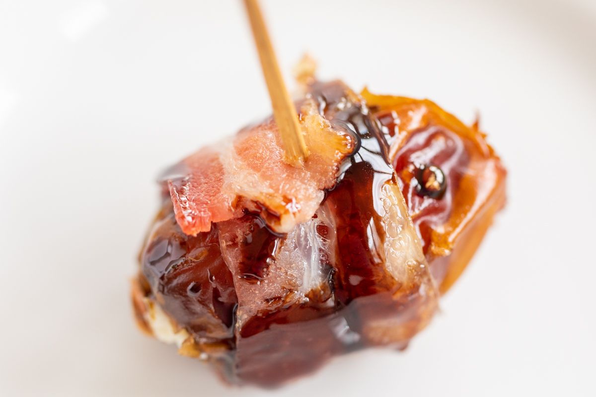 A close up of stuffed dates wrapped in bacon and drizzled in balsamic glaze.