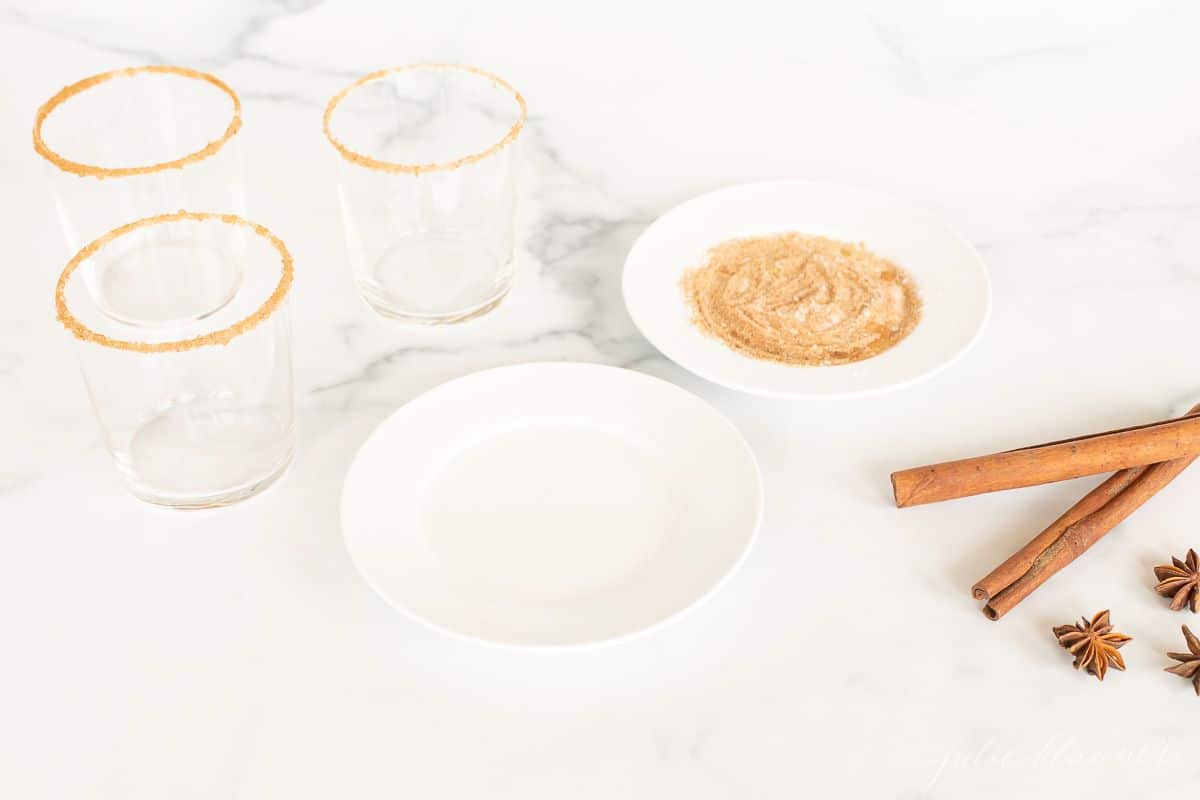 A marble surface with plates and glasses to add a sugared rim to apple cider margaritas.