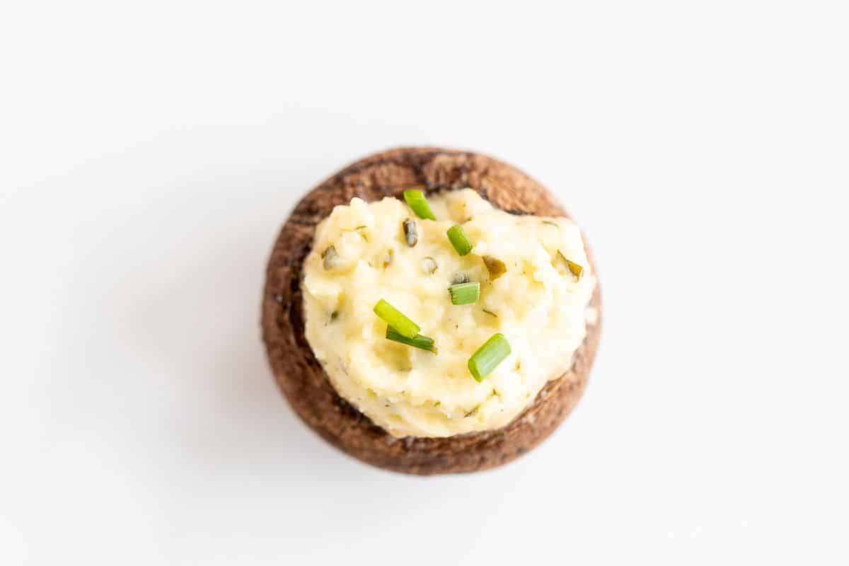 A single boursin stuffed mushroom on a white surface, topped with diced chives.