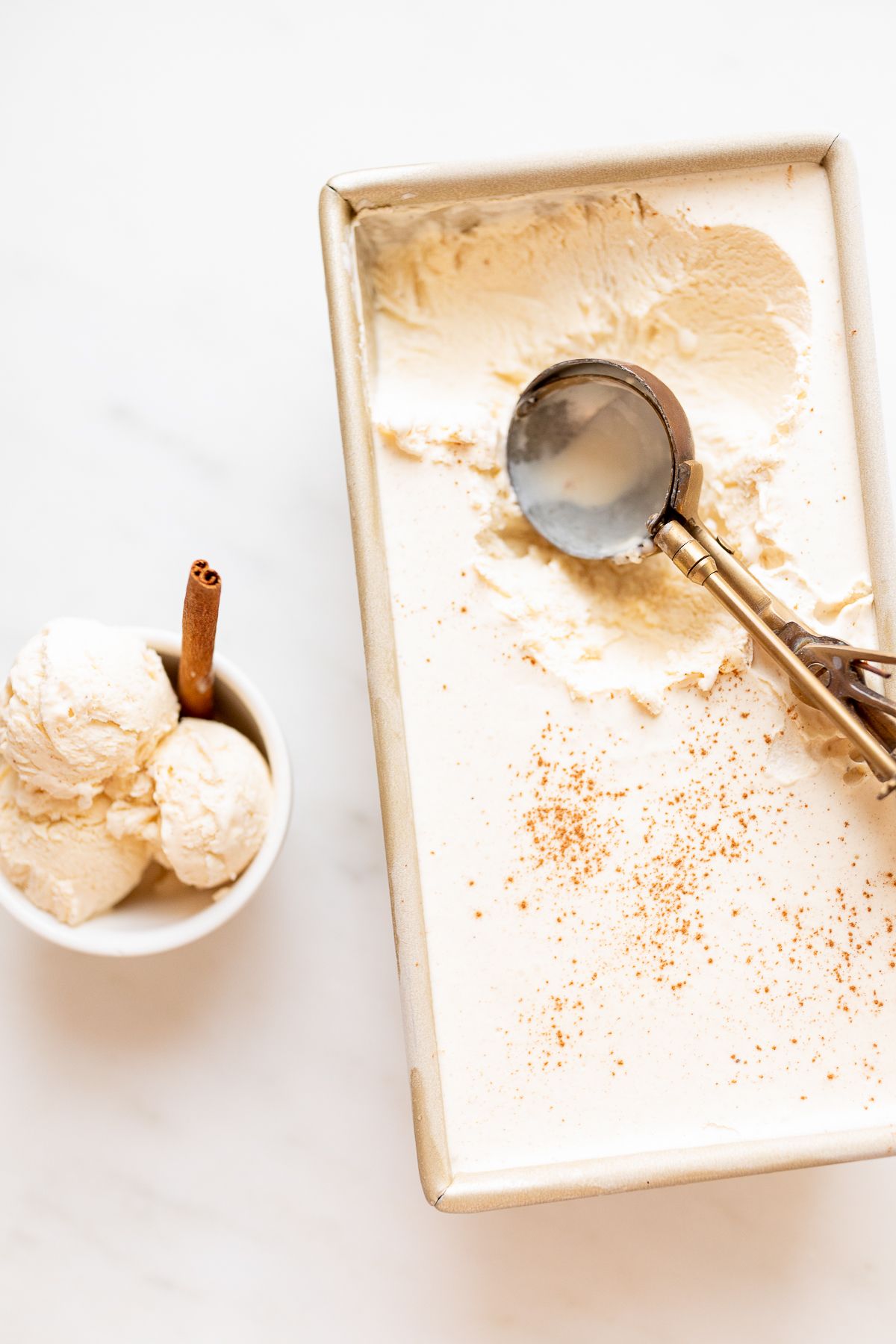 eggnog ice cream served in a small white bowl, with a gold loaf pan full of ice cream in the background.