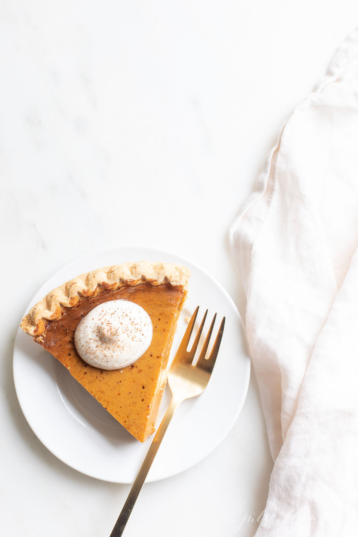 A slice of pumpkin pie with a dollop of eggnog whipped cream on top.  