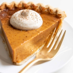 A slice of pumpkin pie with a dollop of eggnog whipped cream on top.