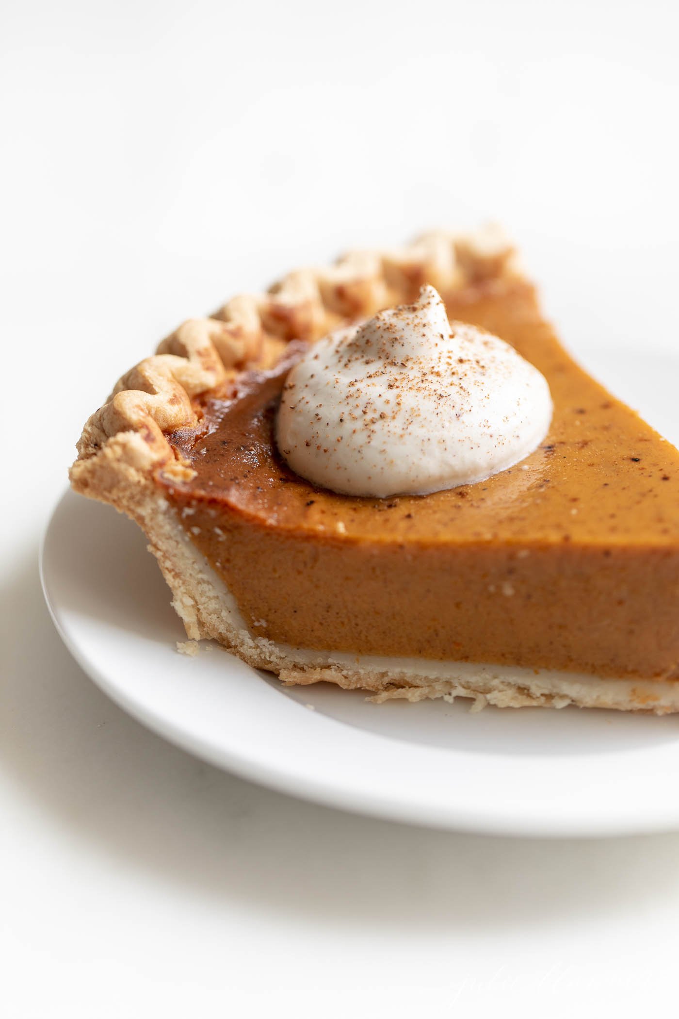A slice of pumpkin pie with a dollop of eggnog whipped cream on top.