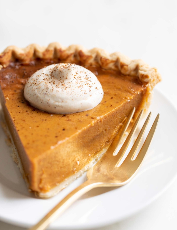 A slice of pumpkin pie with a dollop of eggnog whipped cream on top.