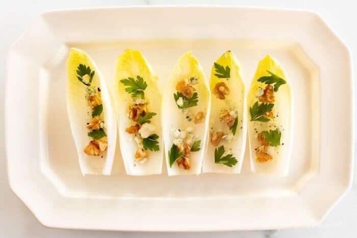 A white platter with individual endive lettuce leaves, filled with nuts, cheese and more for an endive salad appetizer.