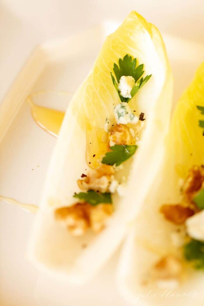 Individual endive lettuce appetizers on a white platter, drizzled with honey.