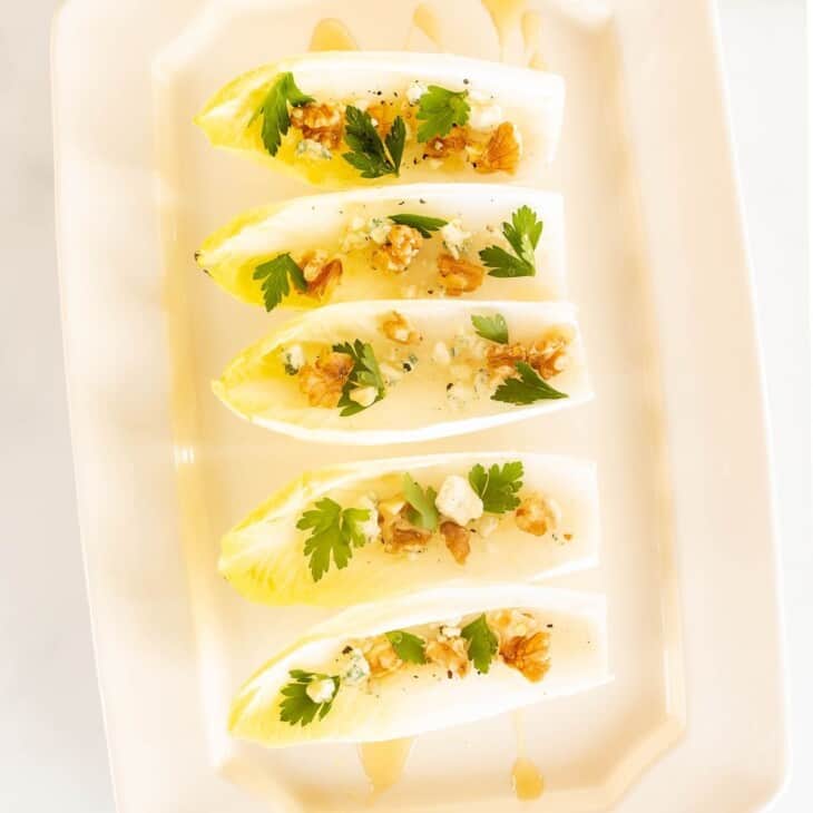 A white platter with individual endive lettuce leaves, filled with nuts, cheese and more for an endive salad appetizer.