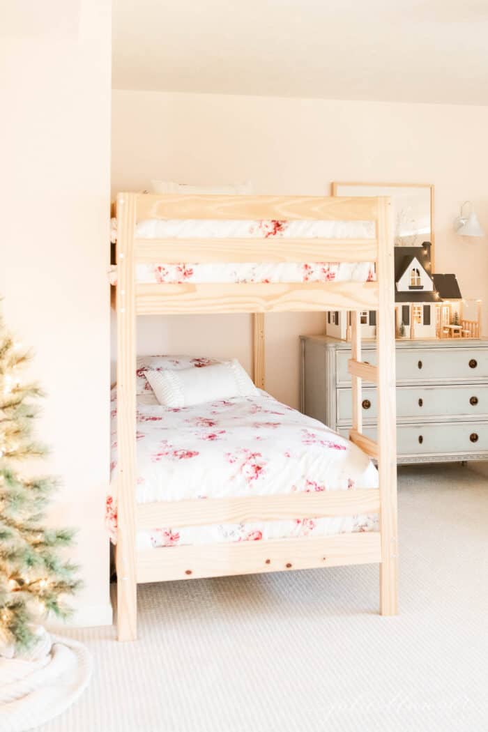 A little girls' room with bunk beds and a blue chest of drawers topped with a dollhouse decorated for Christmas.