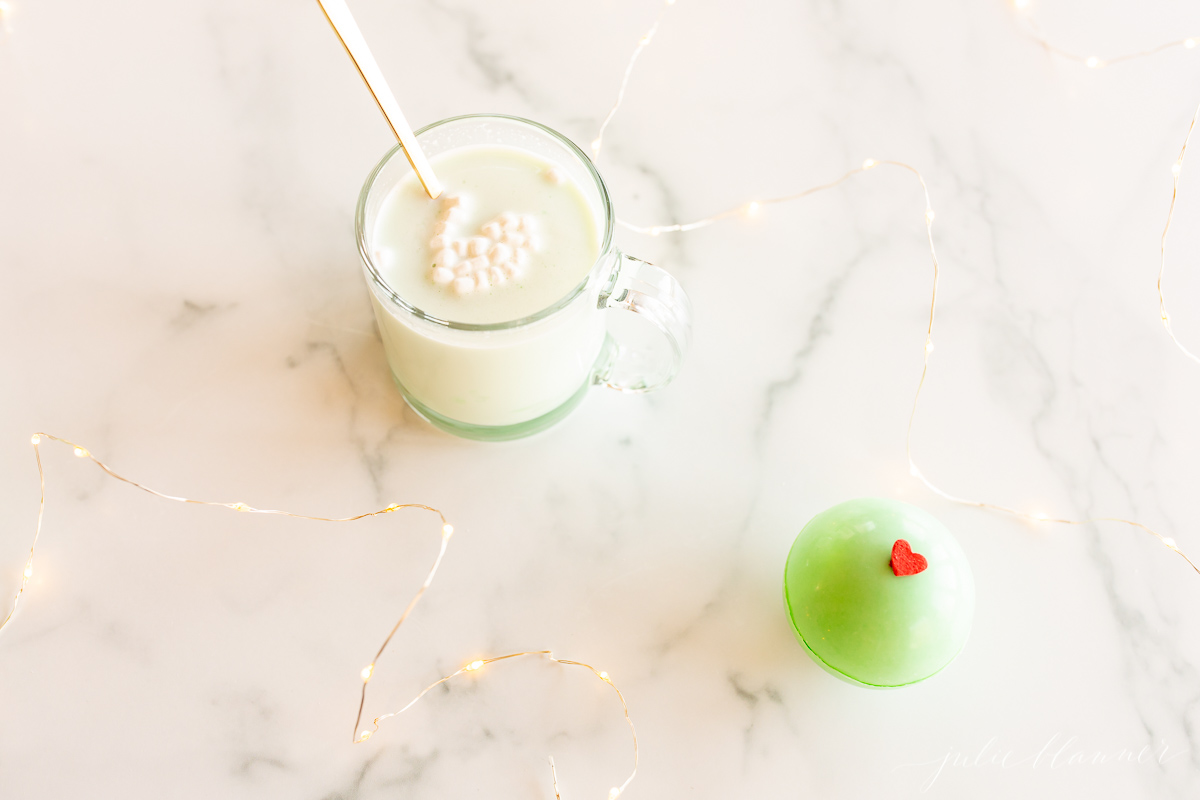 A cup of hot cocoa with whipped cream and a green Grinch hot chocolate bomb.