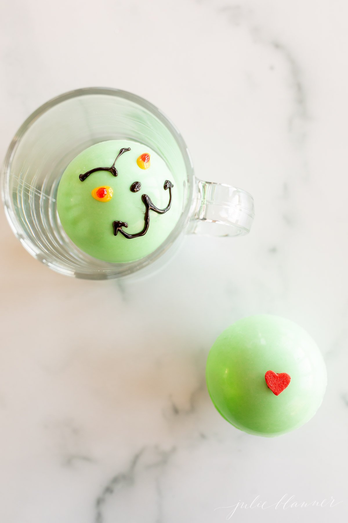 A Grinch hot chocolate bomb next to a cup.