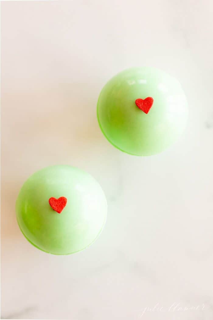 green grinch hot chocolate bombs decorated with red hearts, on a marble surface.