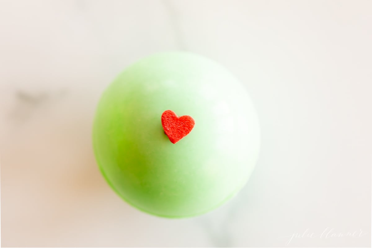 A grinch hot chocolate bomb with a red heart on it