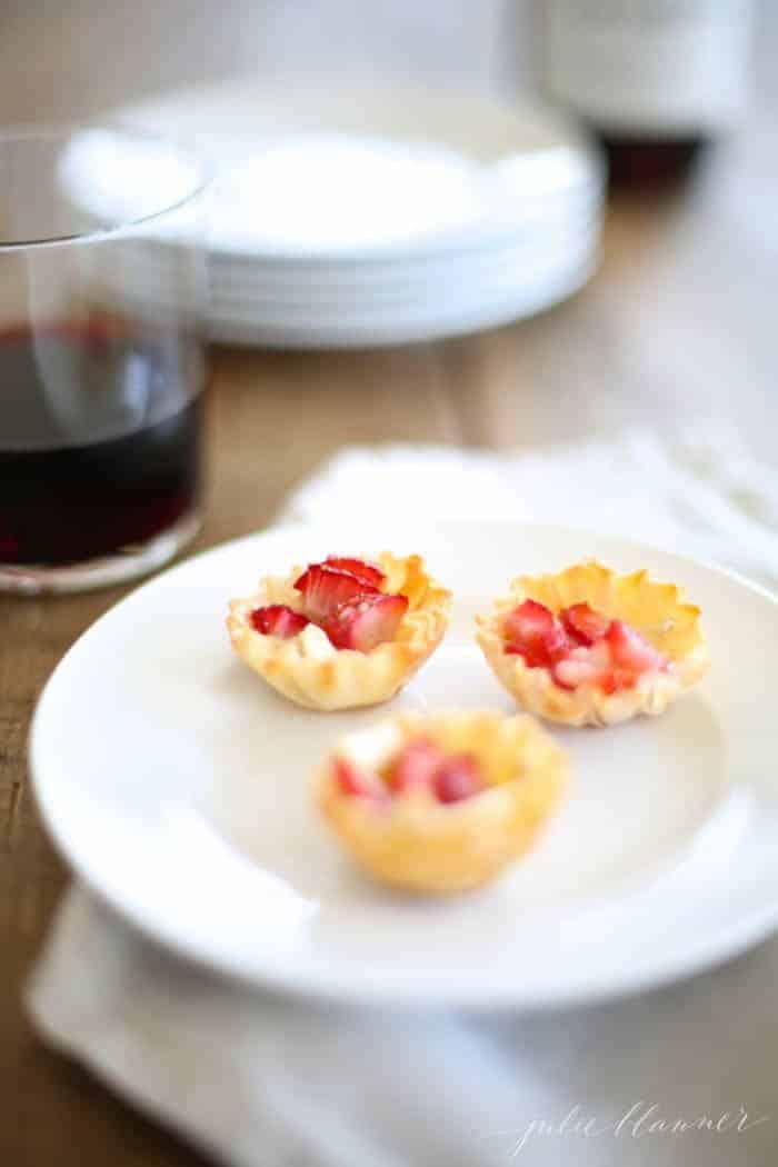 A white plate with small brie and strawberry hors d oeuvres.