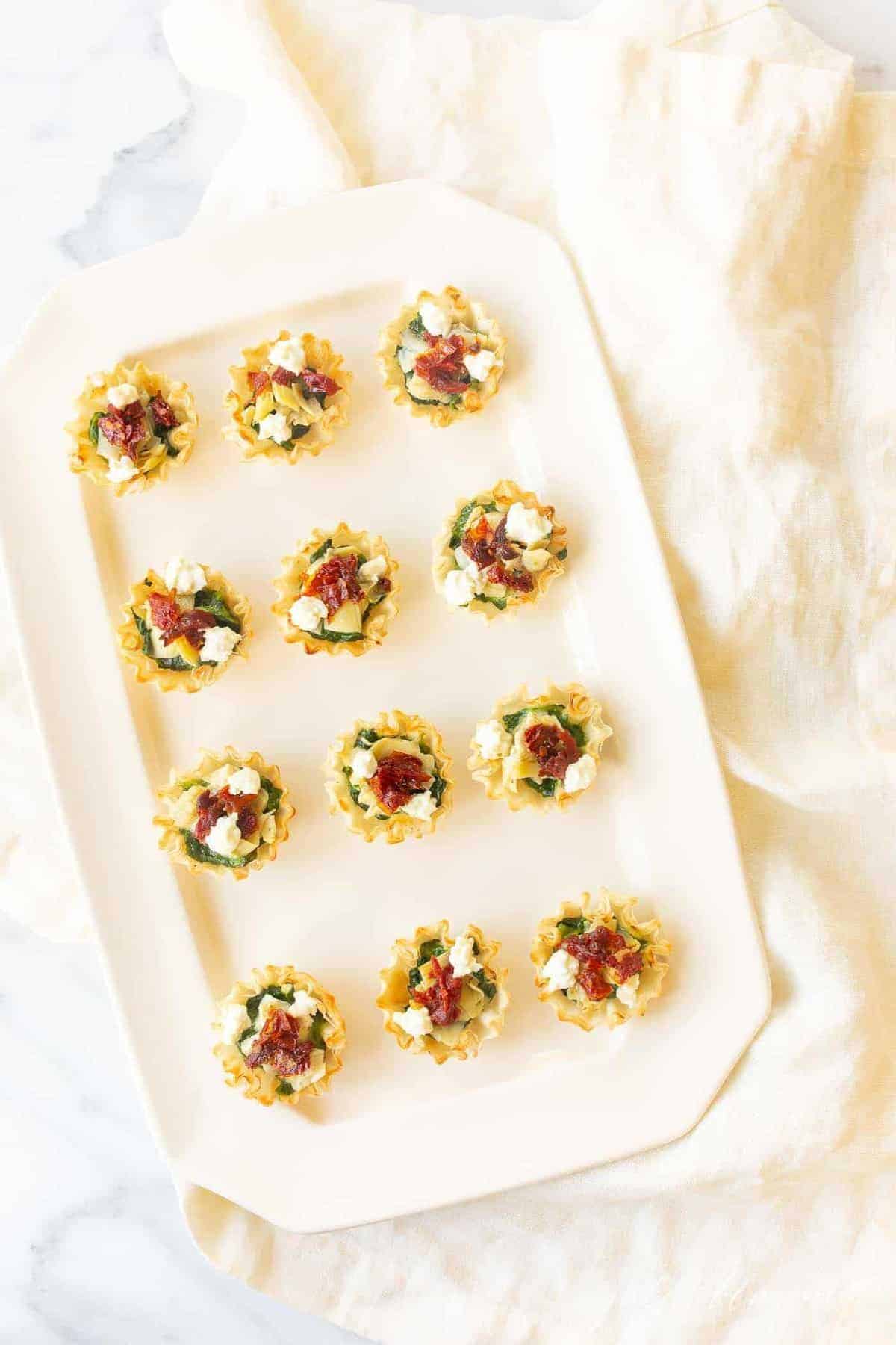 A white rectangular platter featuring phyllo cup hors d'oeuvres.