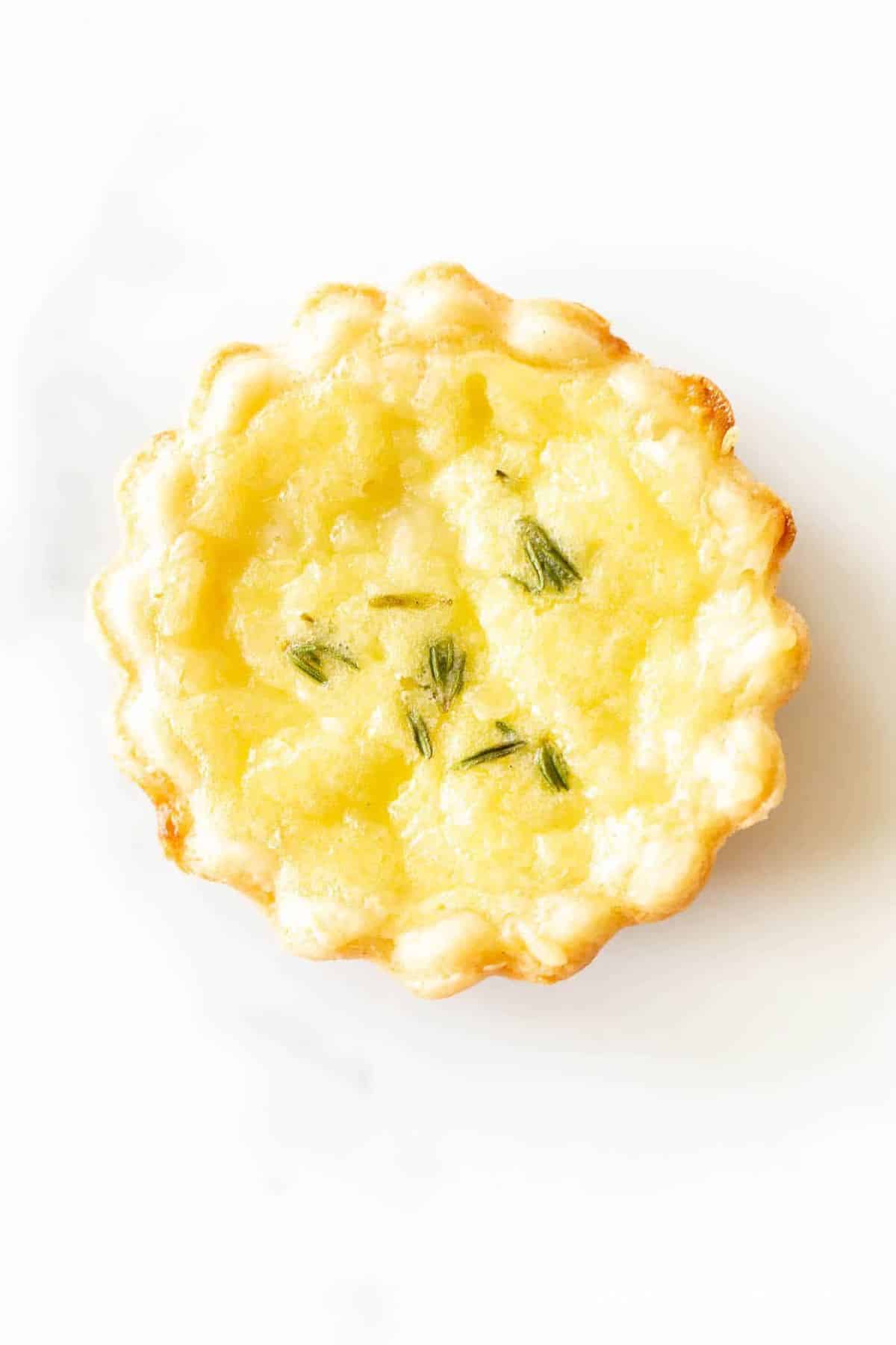 A single miniature cheese tart hors doeuvre on a white surface.