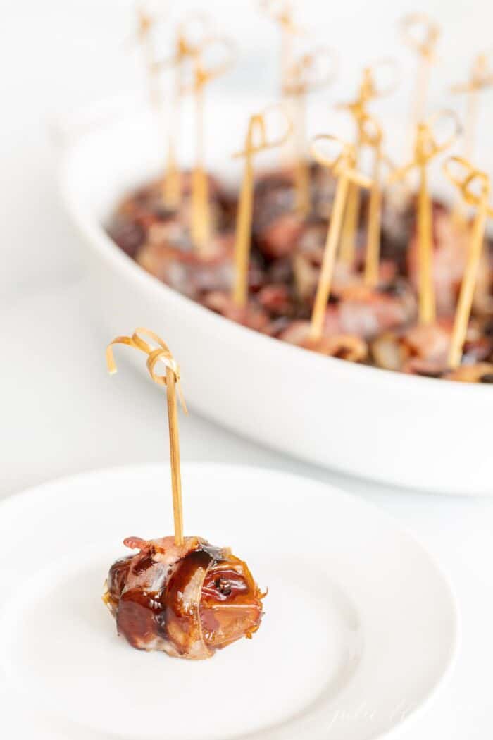 An individual stuffed date with a toothpick on a white plate, baking dish in background.