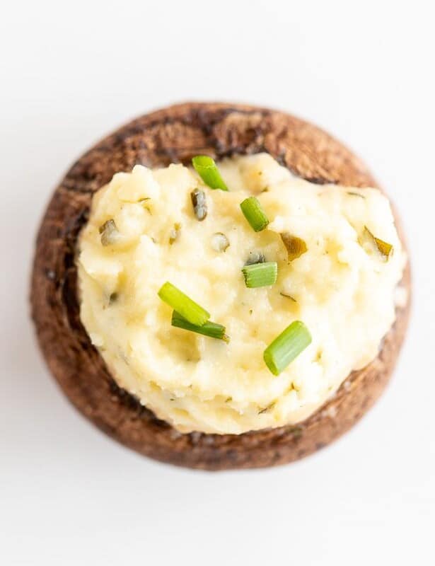 A single boursin stuffed mushroom on a white surface, topped with diced chives.