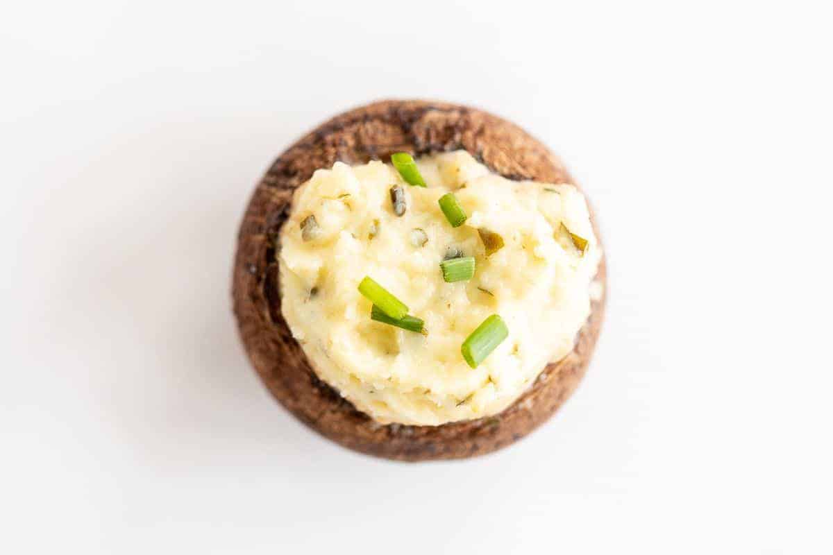 A single boursin stuffed mushroom on a white surface, topped with diced chives.