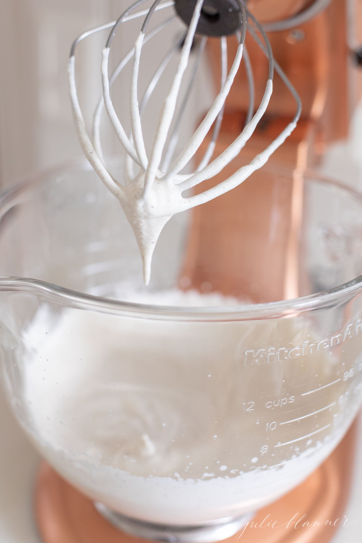 Eggnog whipped cream in the glass bowl of a copper stand mixer.