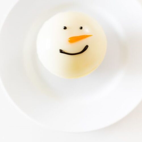 A snowman hot chocolate bomb on a white plate.