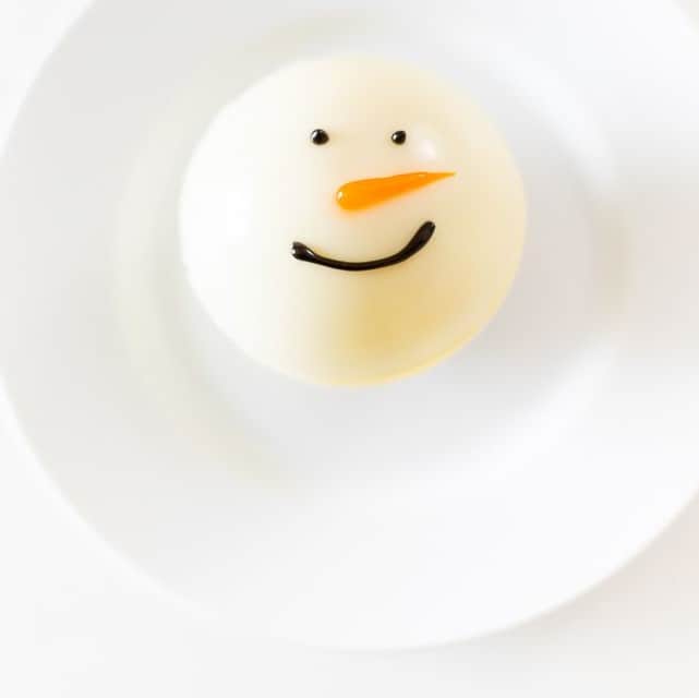 A snowman hot chocolate bomb on a white plate.