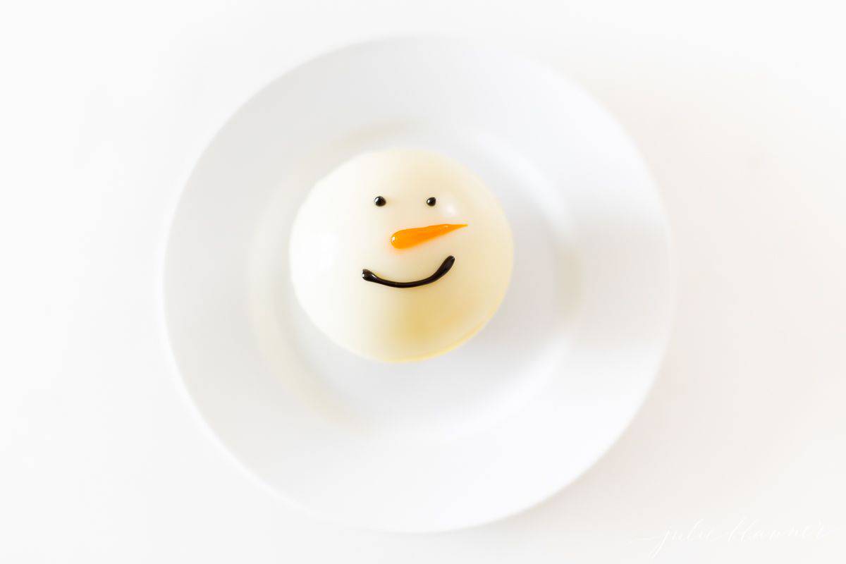 A snowman white hot chocolate bomb on a white plate.