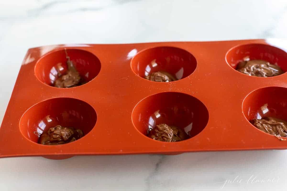 A red silicone sphere mold filled with chocolate for Mexican hot chocolate bombs.