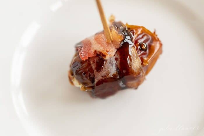 A single stuffed date on a white plate with a toothpick.