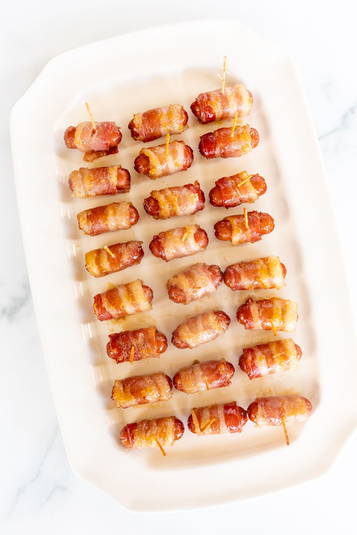 A white tray with bacon wrapped little smokies.