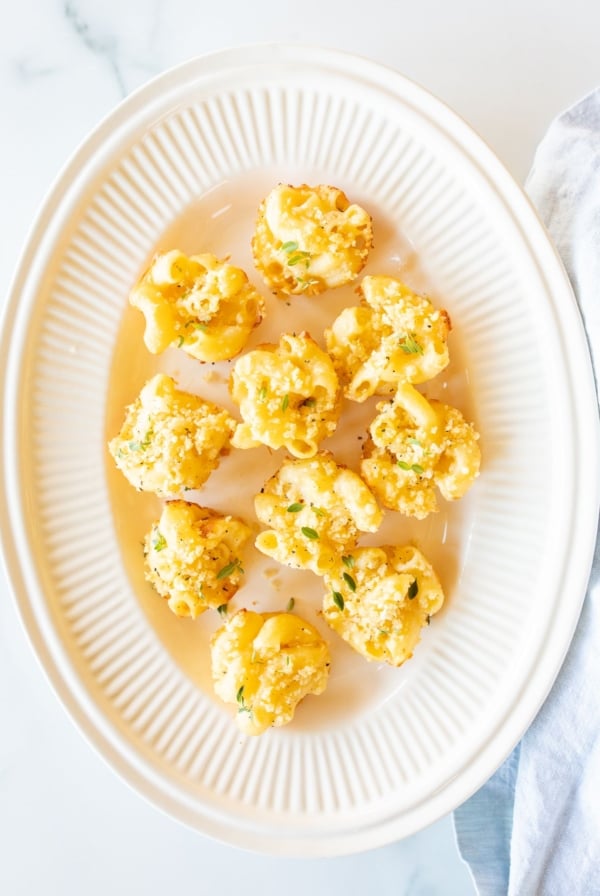 A white oval platter full of mini mac and cheese cups for an appetizer.