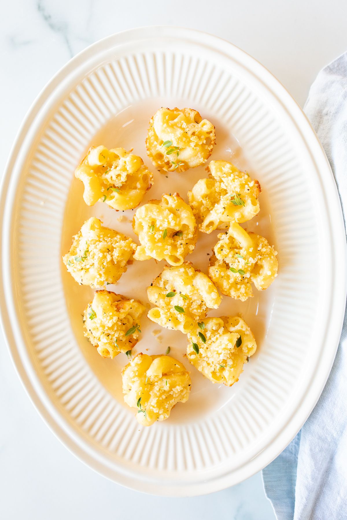 A white oval platter full of mini mac and cheese cups for an appetizer. 